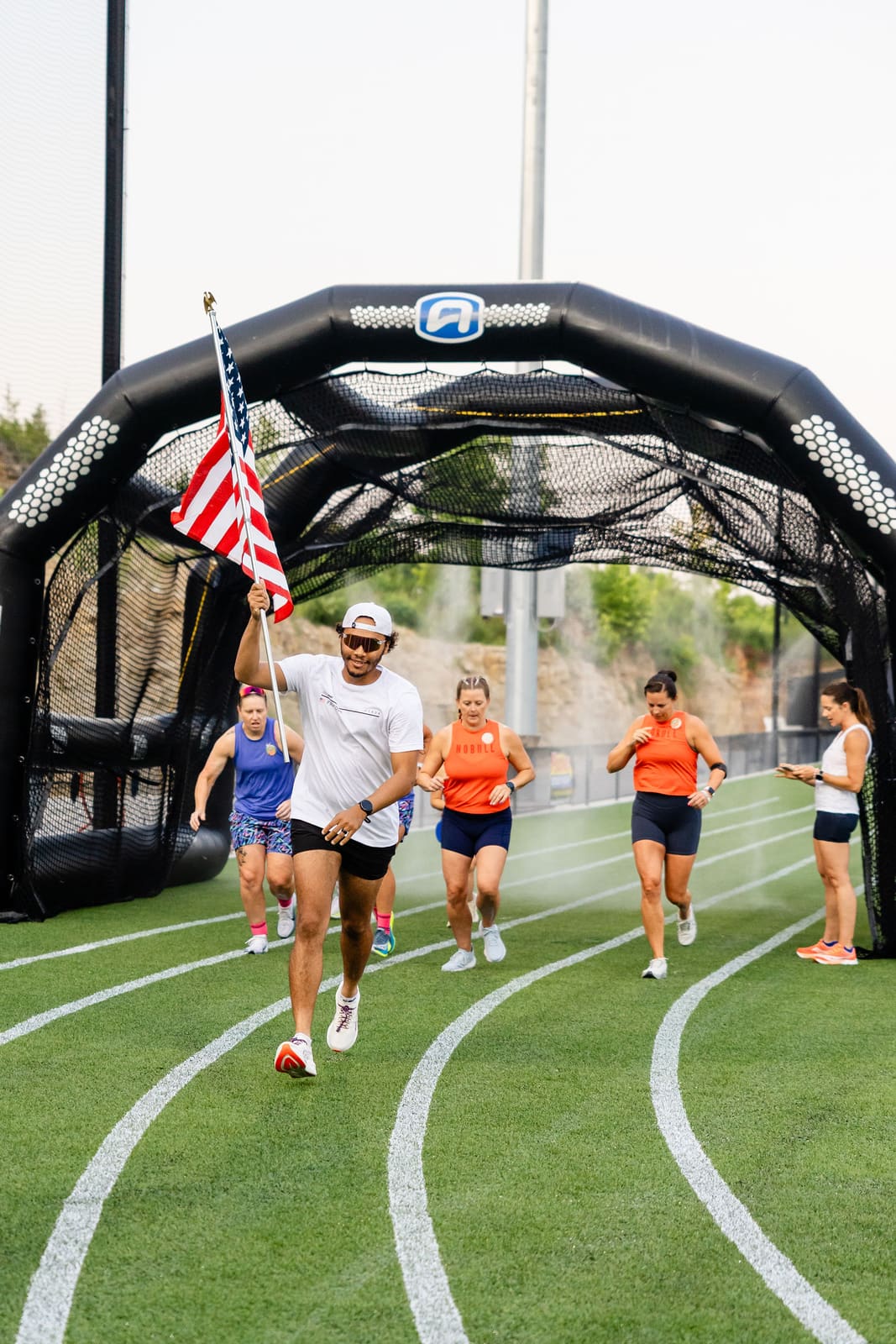 Athletes running through the arch carrying the American flag